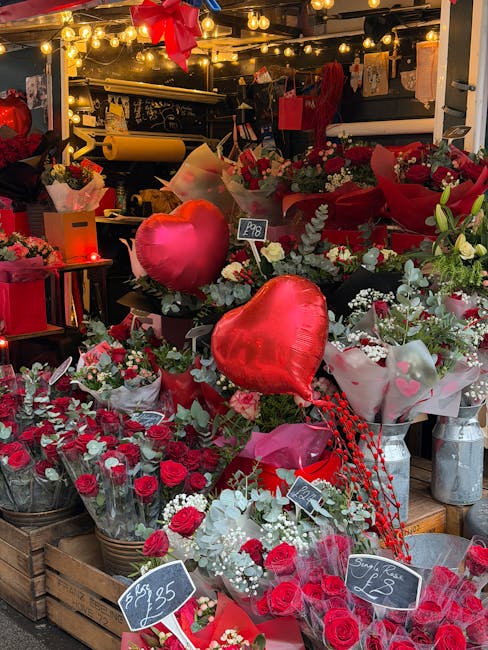 An indoor flower display featuring a variety of fresh floral arrangements predominantly in red and white, including roses, carnations, and baby's breath, with some bouquets wrapped in pink, red, and w