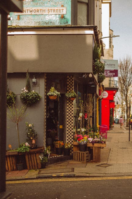 The image shows a florist shop front on a city street, with various floral displays arranged outside. Several bouquets and potted plants feature a mix of colorful flowers including pink, yellow, and p